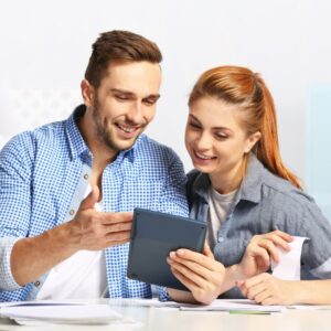 a couple looking happily at a tablet and paperwork