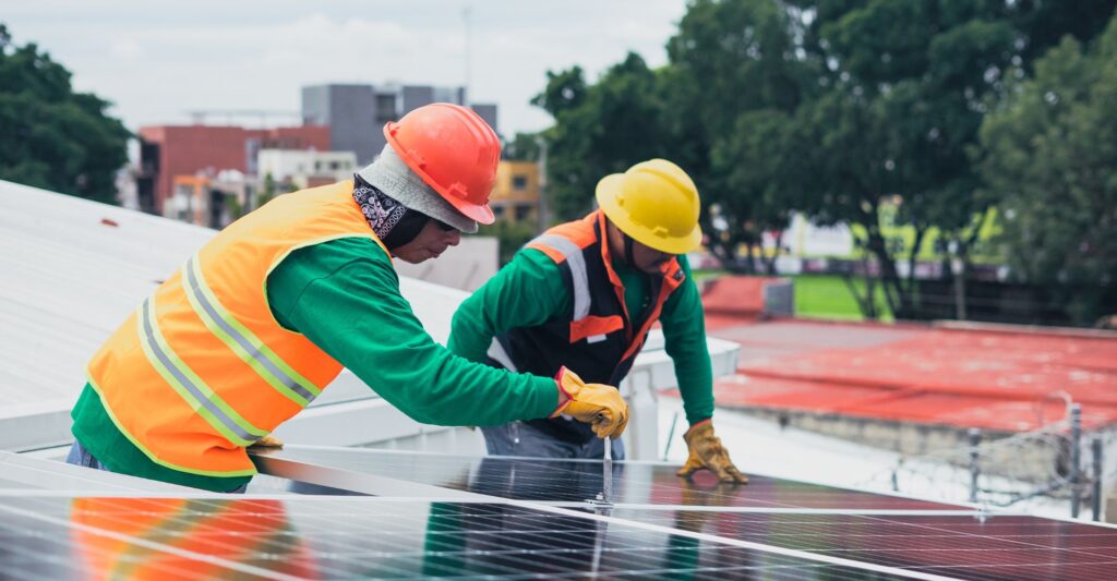 people in safety gear setting up solar panels on a roof