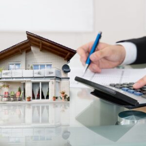 person making calculations on calculator in front of toy model home
